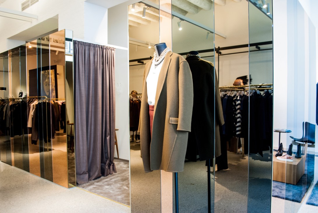 Interior of Bungalow menswear and womenswear shop in Stuttgart featuring a camel coat on a mannequin and clothing displays behind glass.