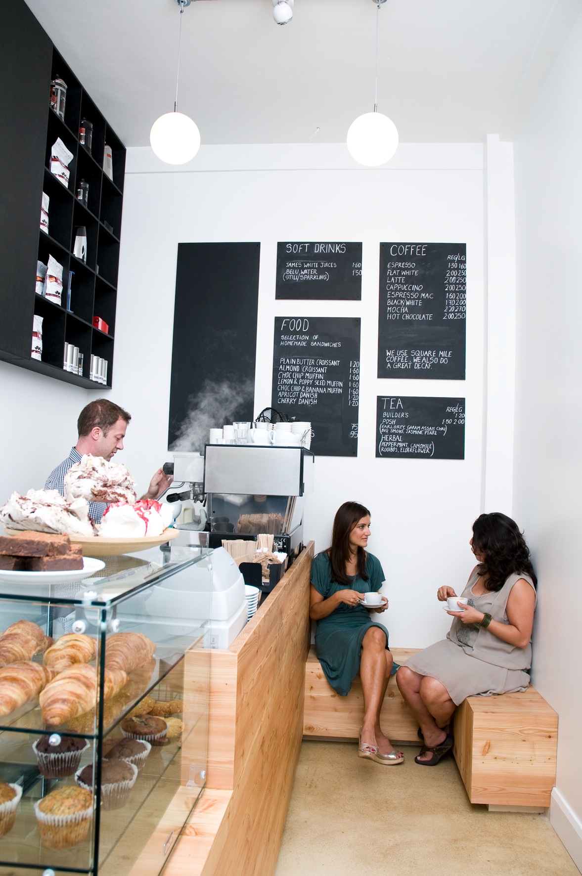 The Espresso Room in Bloomsbury with customers at wooden counter, pastries in display case, and menu boards on white wall.