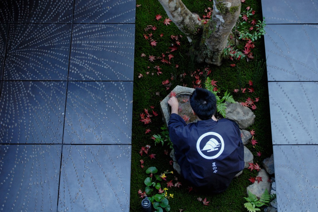 Guest in Hoshinoya branded jacket tending to moss garden with red maple leaves and stones