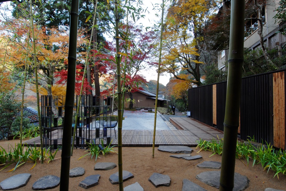 Hoshinoya ryokan courtyard with bamboo, autumn foliage, stone pathways and traditional Japanese architecture.