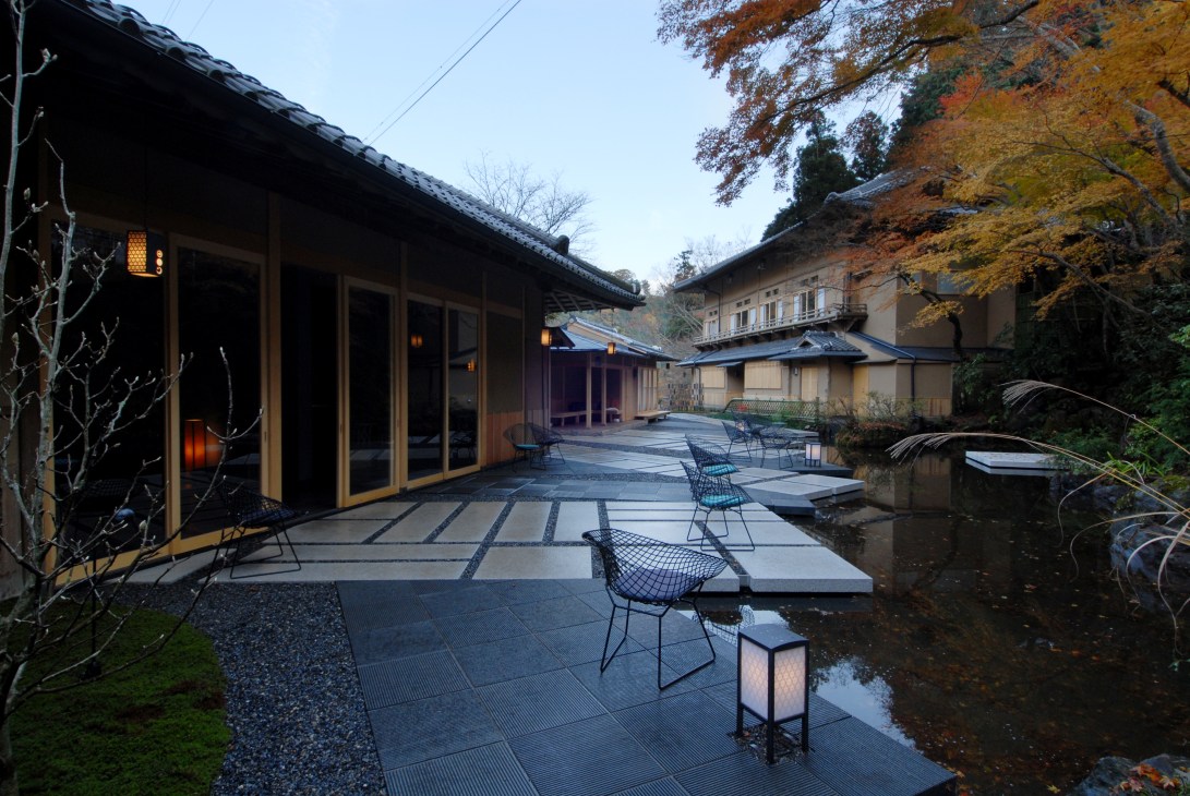 Modern courtyard at Hoshinoya ryokan featuring contemporary patio with metal chairs, traditional Japanese architecture, and autumn foliage.