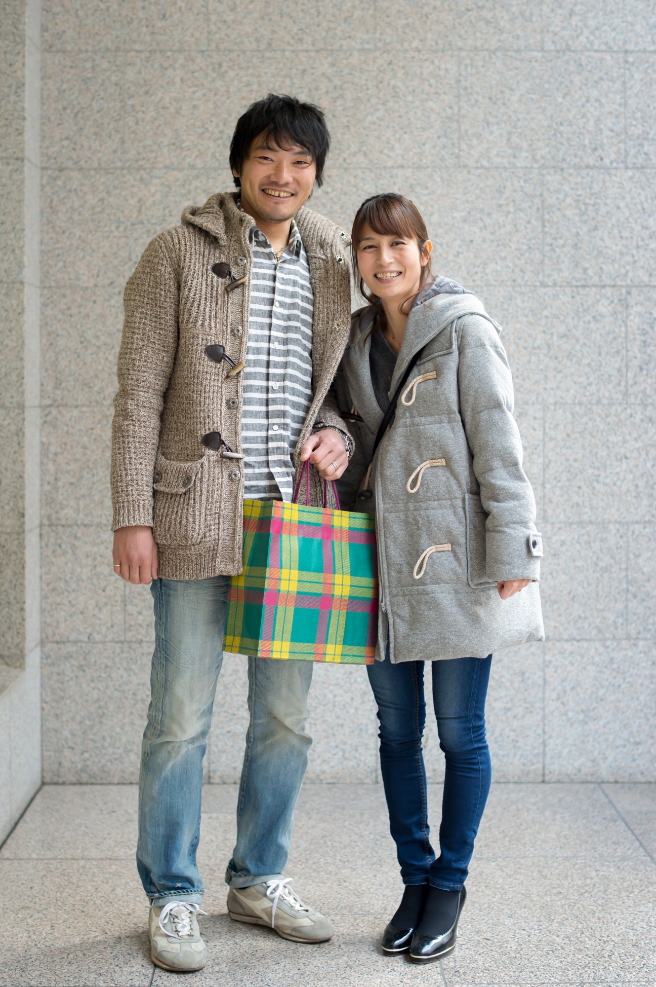 A young couple smiling while holding a tartan shopping bag from Isetan department store.