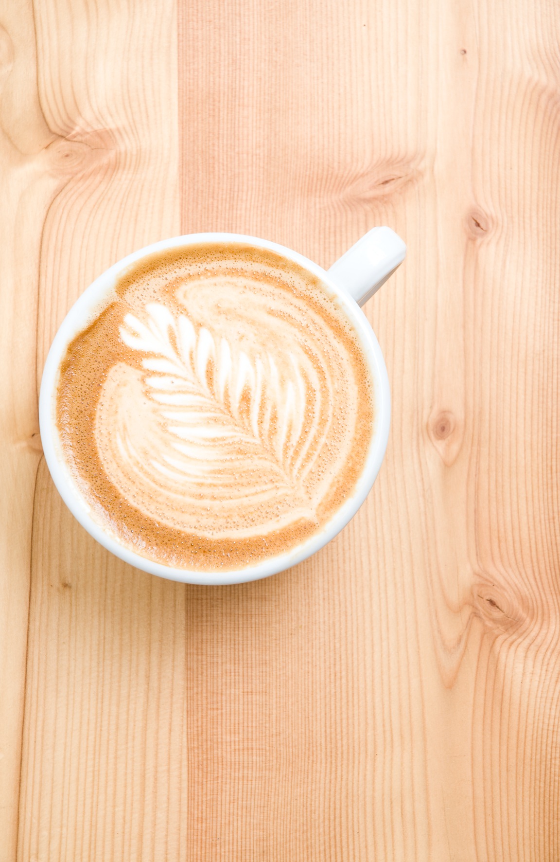 White cup of latte with latte art leaf design on wooden surface