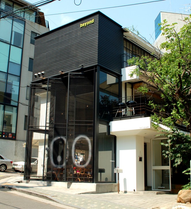 Modern storefront with black corrugated metal siding and large mesh window displays on ground level.