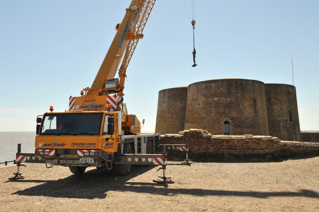 Yellow crane lifting Antony Gormley's iron sculpture Check onto Aldeburgh's Martello Tower.