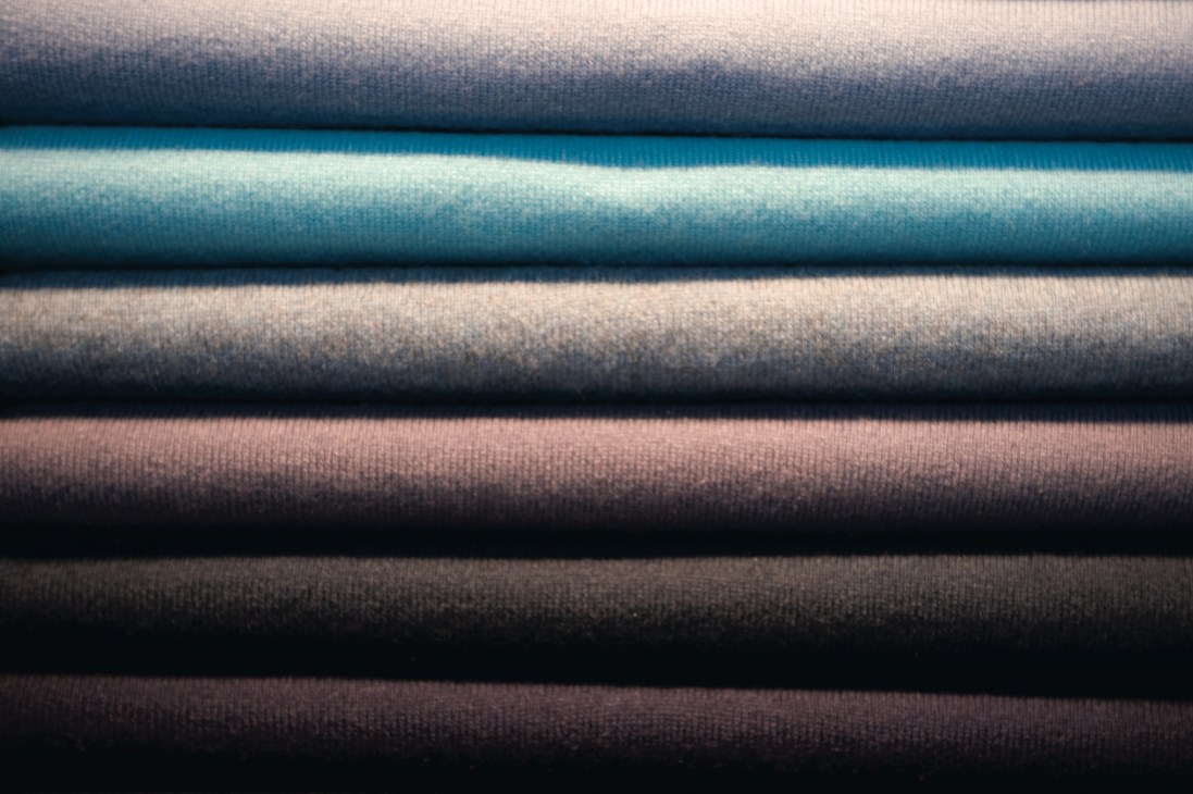 Rolled cashmere fabric swatches in navy, turquoise, grey, mauve and black.