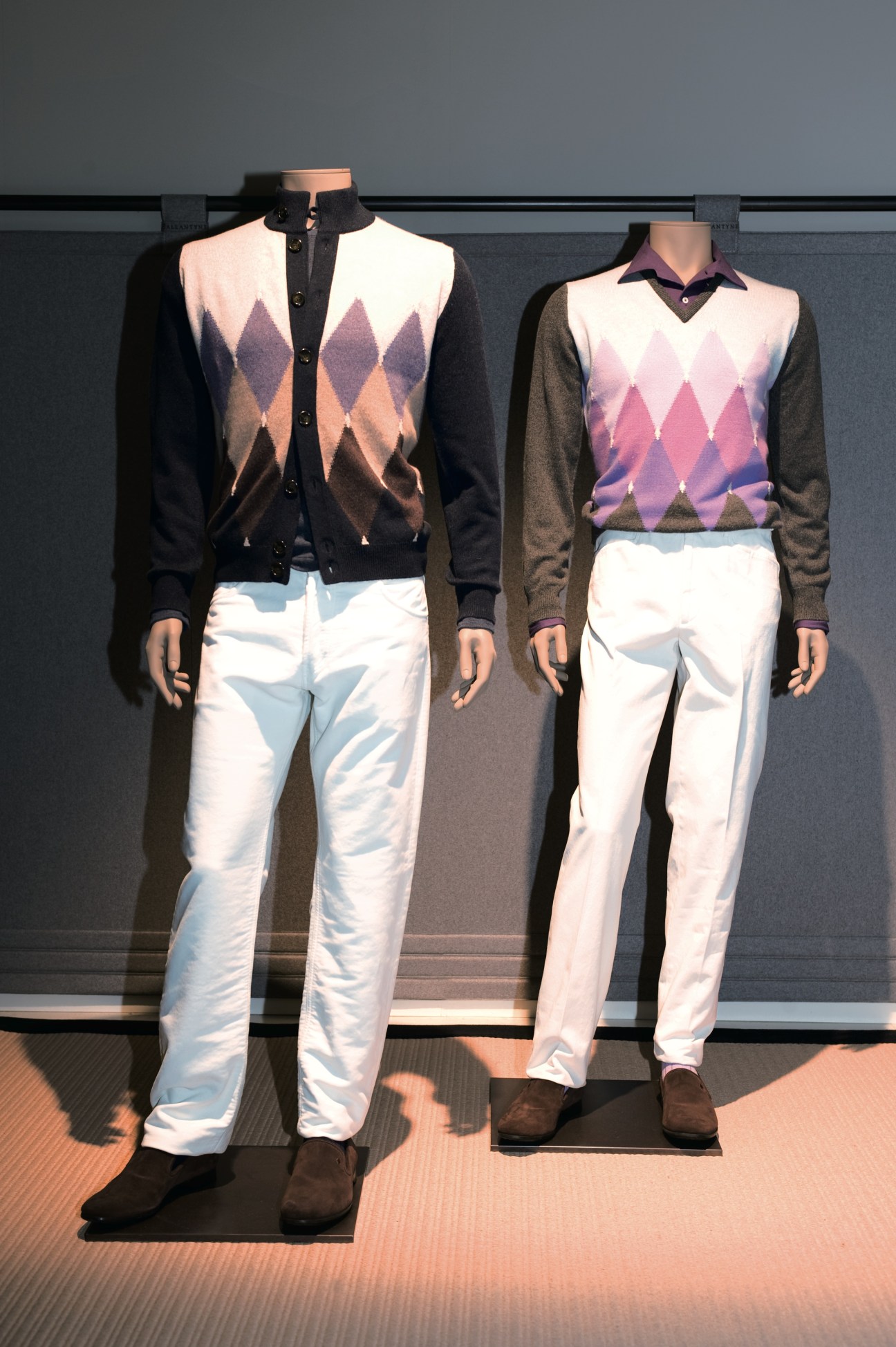 Two mannequins displaying Ballantyne's argyle cardigans and sweaters paired with white trousers.