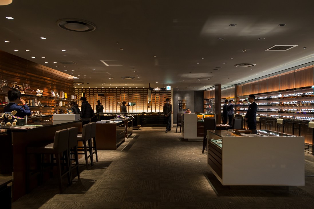 Interior of Isetan men's annex Residence floor showing luxury retail space with wooden shelving, display cases, and customers browsing.