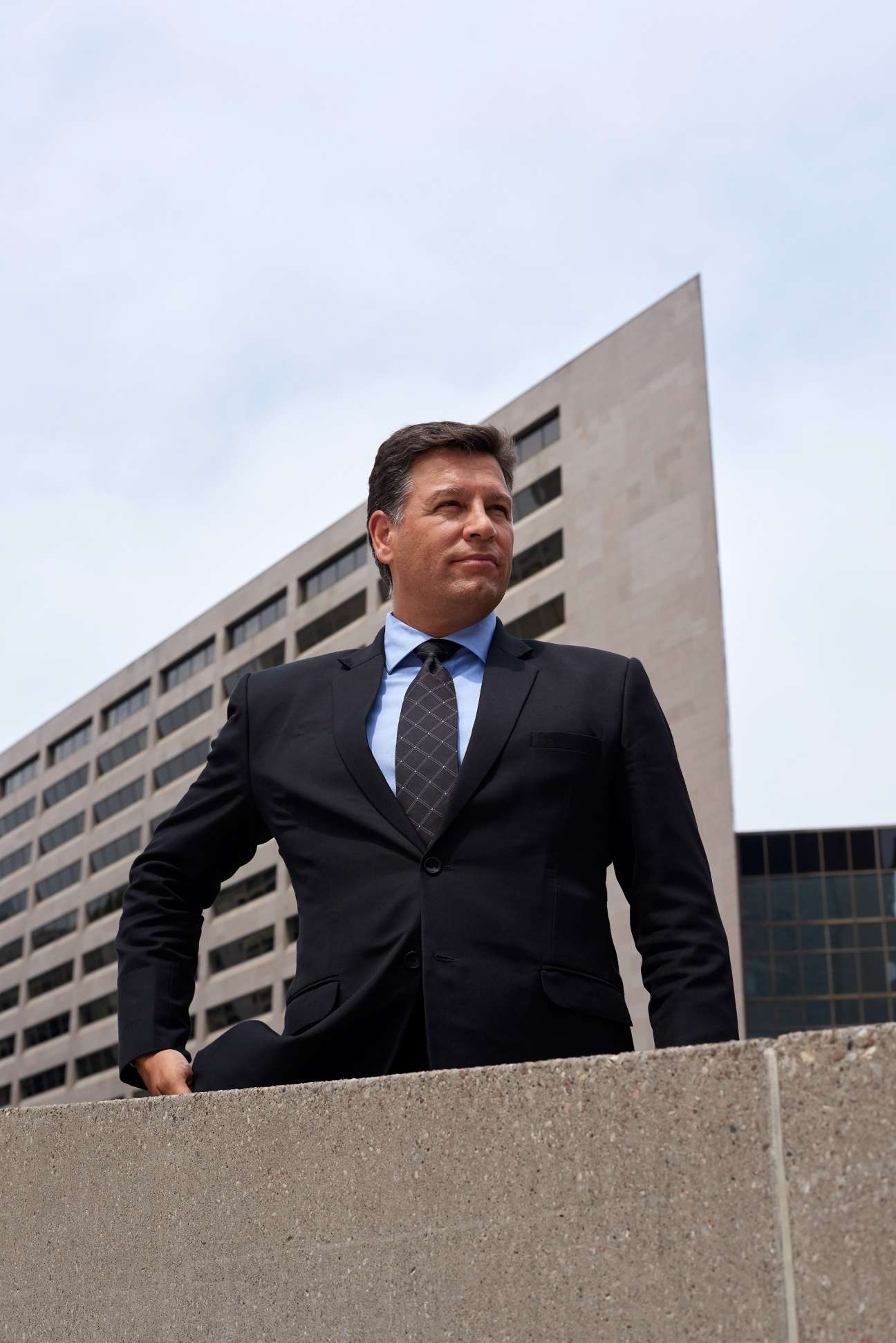 Man in dark business suit and tie standing in front of modern concrete building.