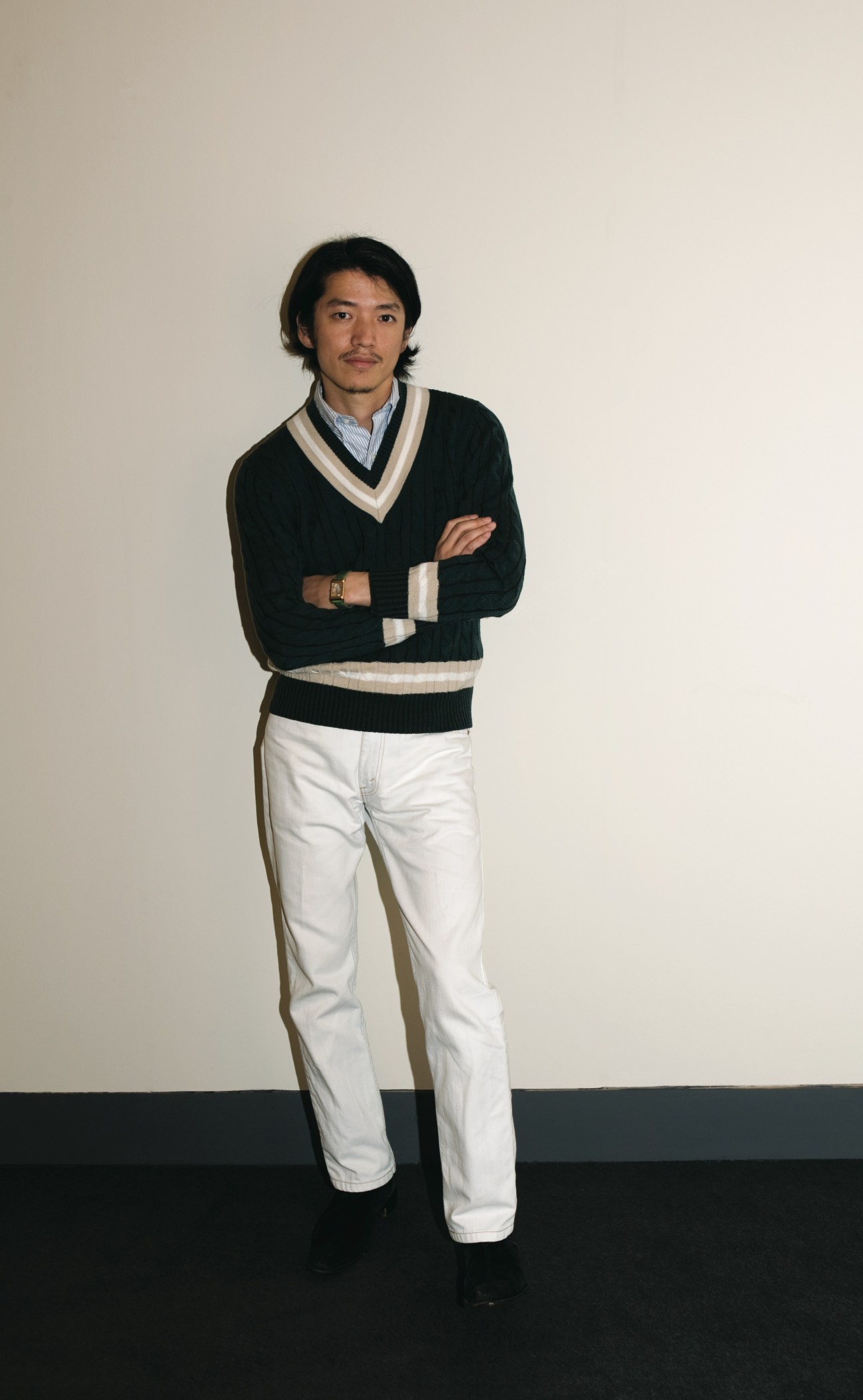 Masahiko Sakata, Men's Bigi designer, wearing a black and white V-neck sweater, light blue shirt, white jeans, and watch.