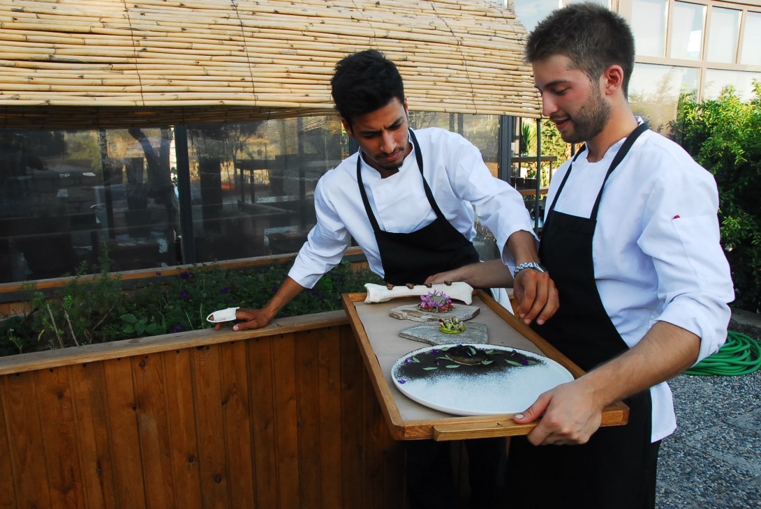 Two chefs in white shirts and black aprons present a plated dish at Alancha restaurant in Turkey.