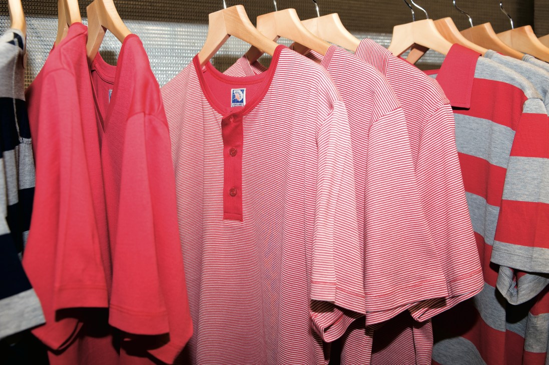 Bright red and striped T-shirts and pink garments hanging on wooden hangers displayed on a rack.