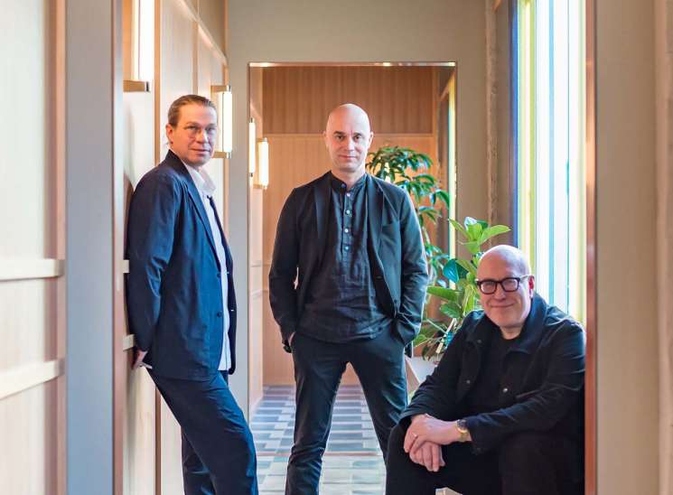 Three men standing in a modern hotel corridor with geometric patterned flooring and warm lighting