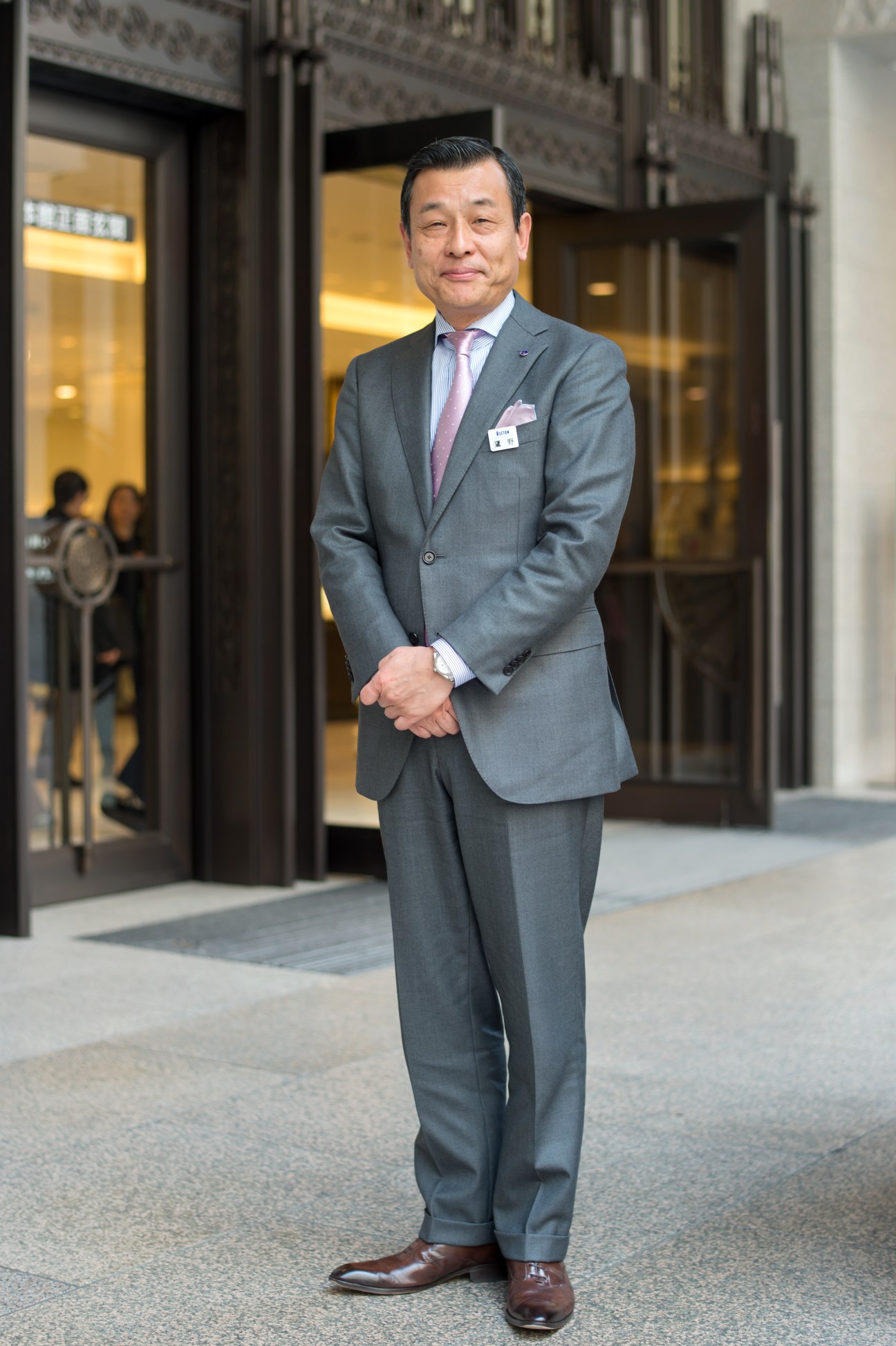 Masaaki Takano, general manager of Shinjuku Isetan, stands outside the store entrance in a grey suit.