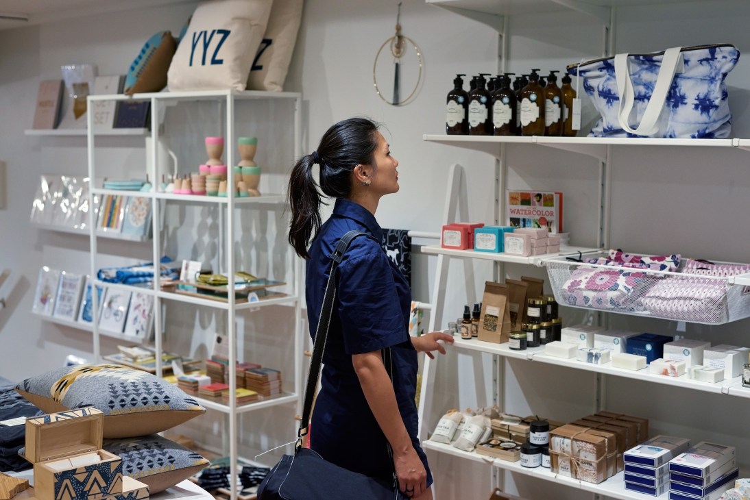 Woman browsing artisanal products displayed on white shelves in a bright retail space.