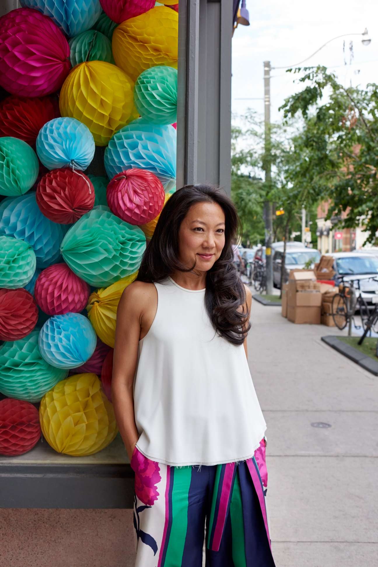 Jen Lee Coss, founder of Brika, stands in front of colorful paper lanterns on a city street.
