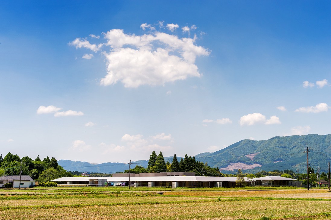 Ebino Ryofuen nursing home nestled in a valley with rice paddies and Kirishima Mountains in background.