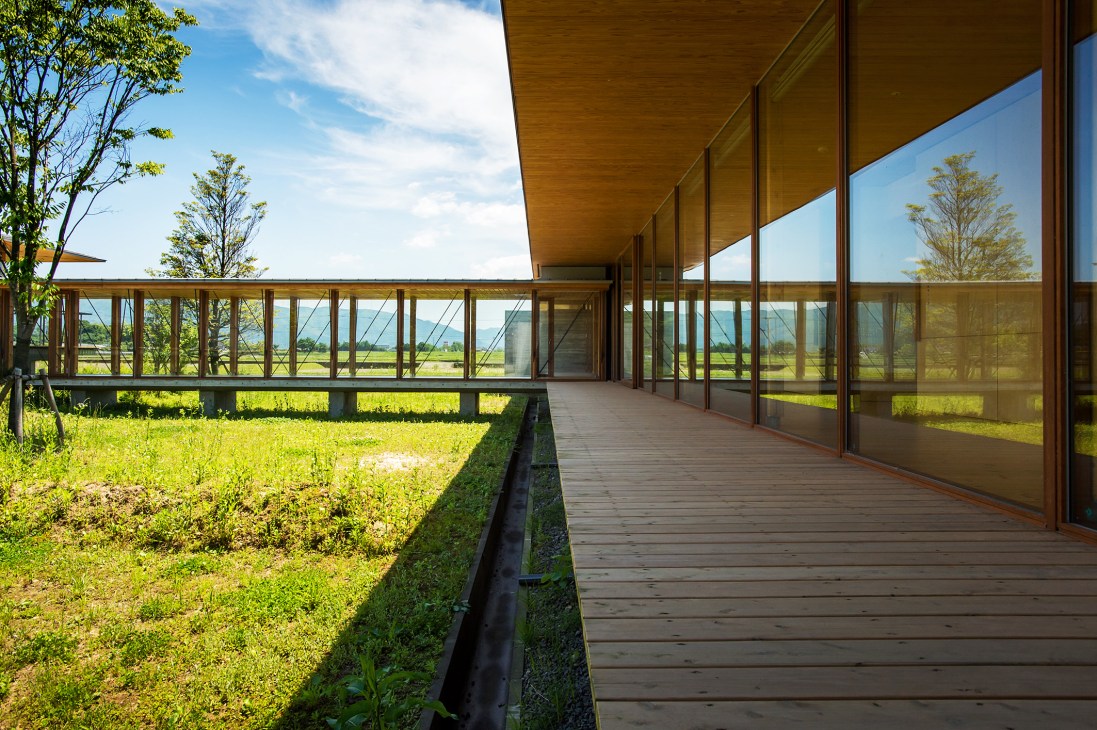 Sun-drenched wooden terrace with floor-to-ceiling windows overlooking rice paddies and mountains at Ebino Ryofuen nursing home.