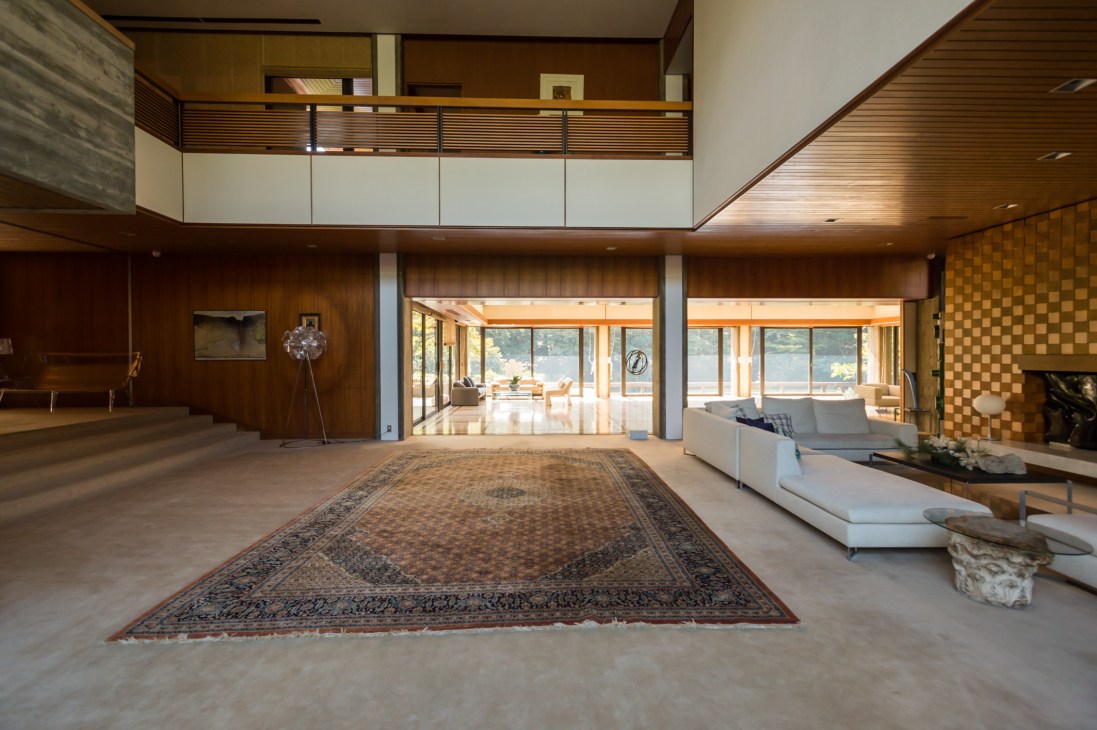 Modern open-plan interior of Italian ambassador's residence with wood paneling, white seating, Persian rug, and views to terrace.