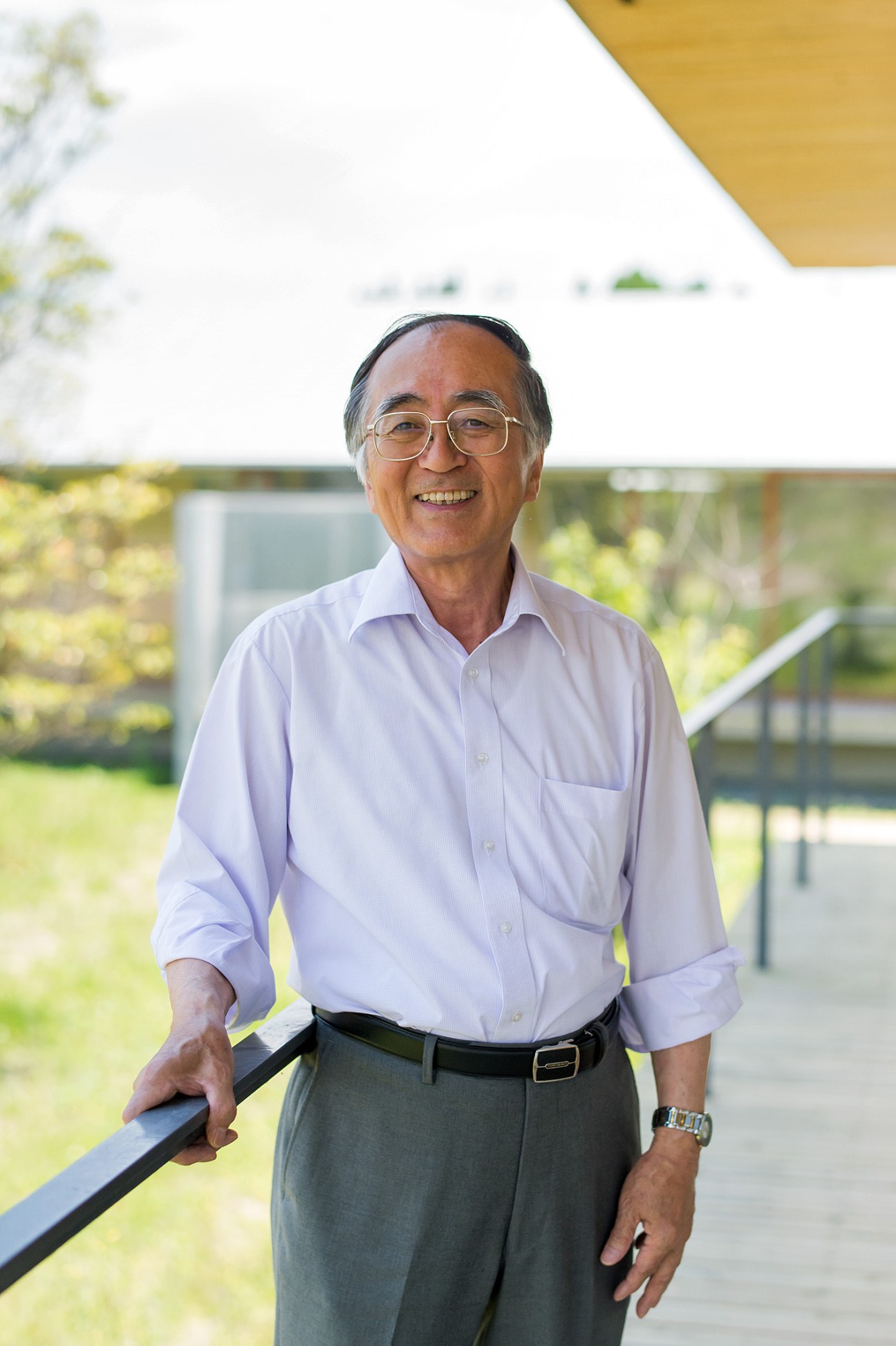 Kimio Shirasaka, manager of Ebino Ryofuen nursing home, stands on a covered terrace overlooking green fields.