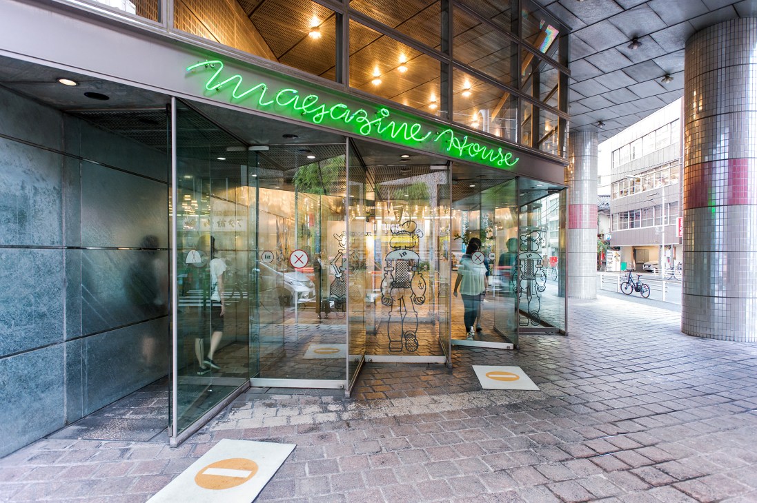 Magazine House storefront with green neon signage on a Tokyo street, featuring glass windows and geometric window displays.