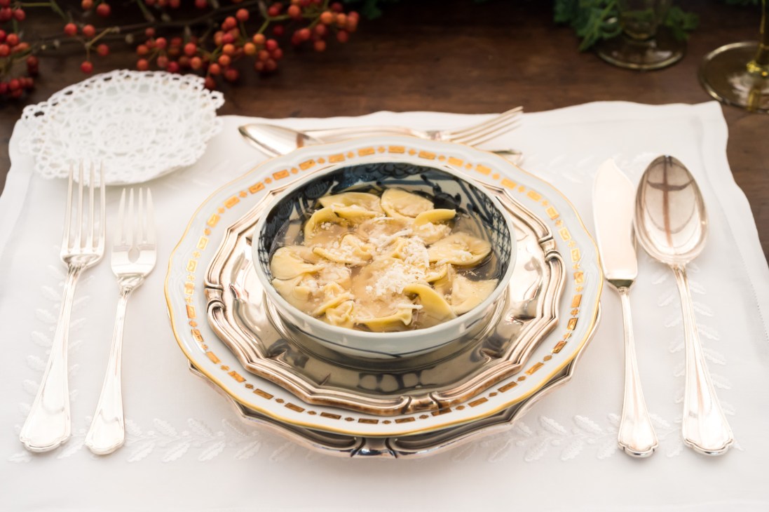 Handmade tortellini served in a decorative black and gold bowl on an ornate plate with antique silverware.