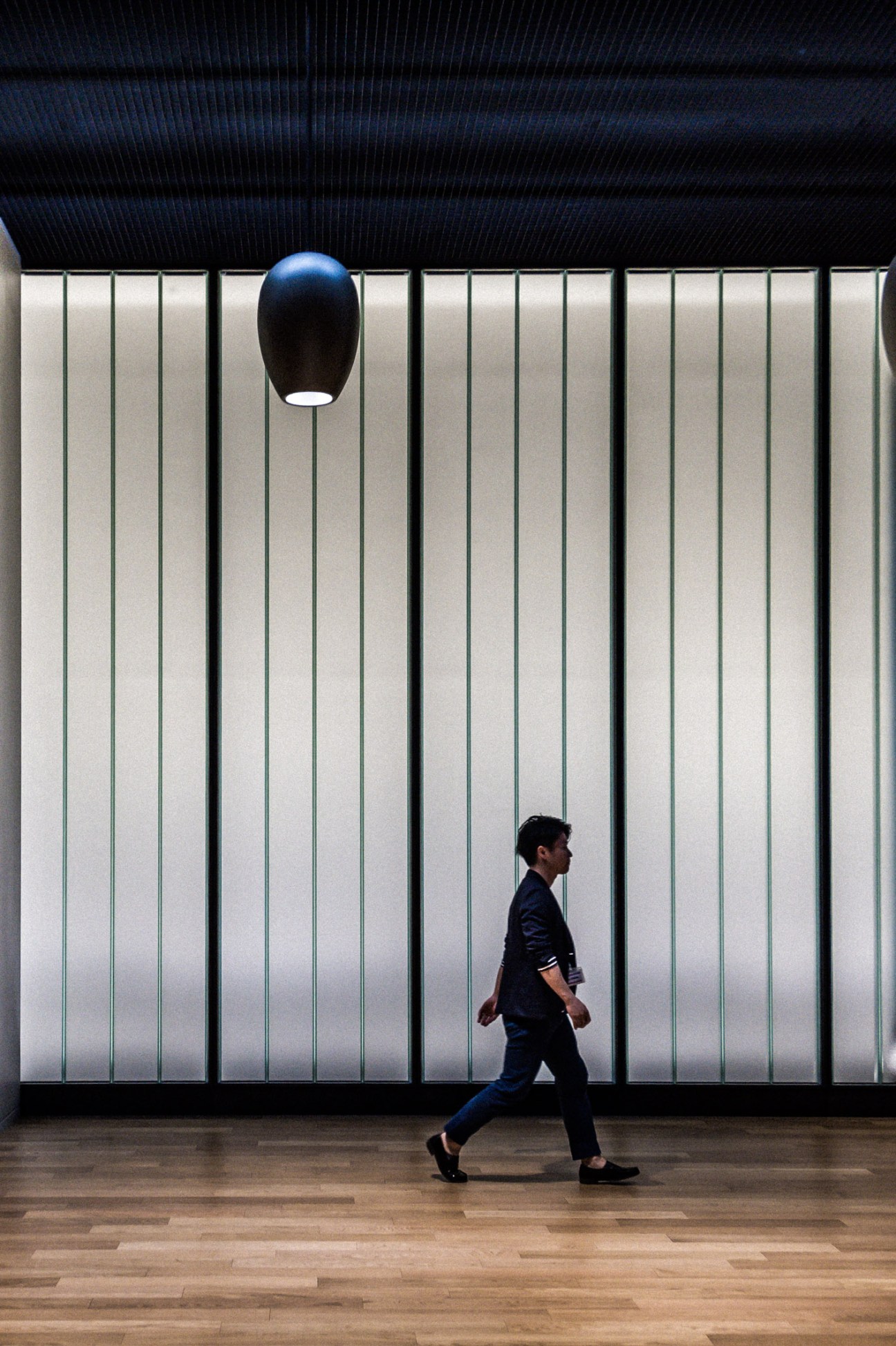 Person walking past floor-to-ceiling windows with vertical ribbing and a spherical black light fixture in Uniqlo City office.