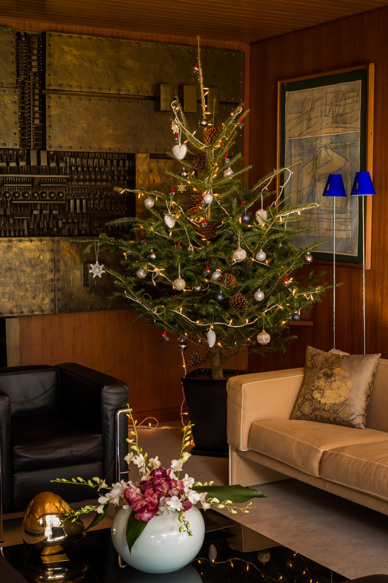 A decorated Christmas tree with ornaments and lights in an elegant wood-paneled room with mid-century furniture.