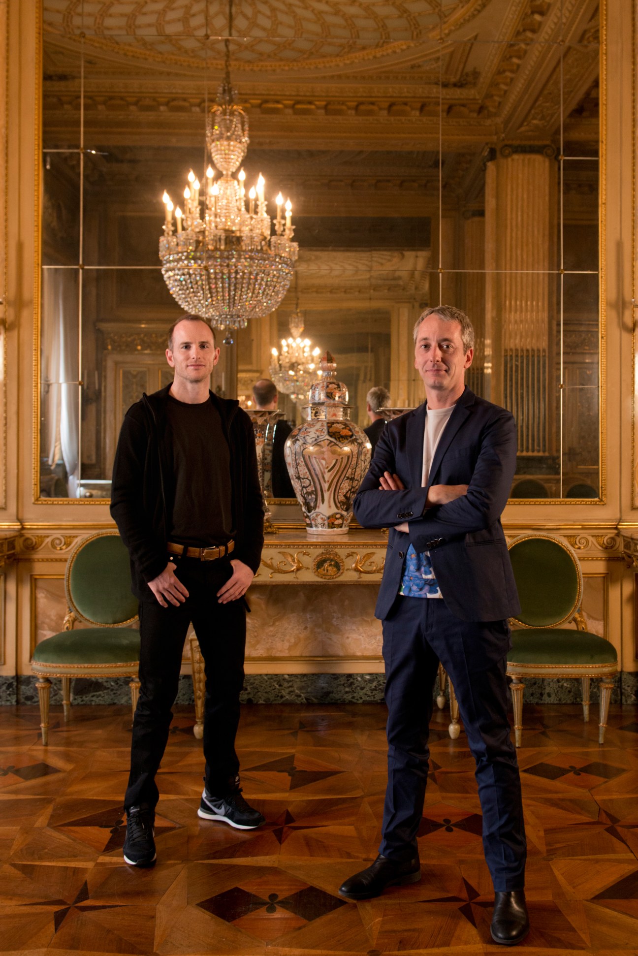 Airbnb co-founder Joe Gebbia and Fabrica design director Sam Baron stand in an ornate palazzo room with crystal chandeliers.
