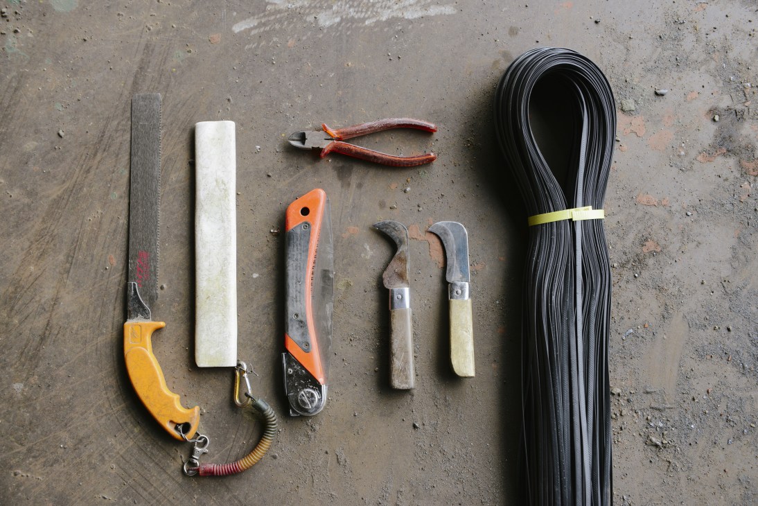 Bamboo scaffolder's toolkit laid out on concrete, including knives, pliers, nylon tie-fasts and coiled black nylon rope.