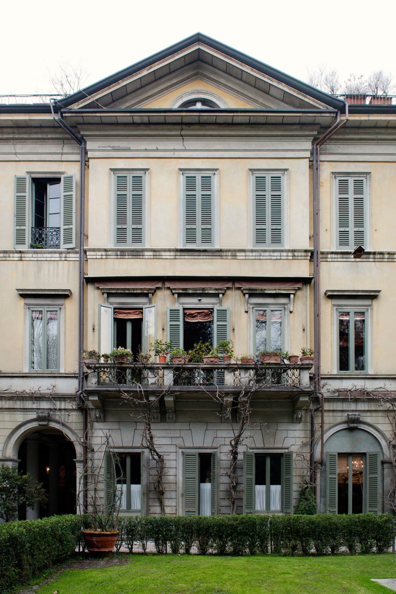 Palazzo Crespi, a cream-colored Italian aristocratic mansion with symmetrical windows, shutters, and a manicured hedge border.
