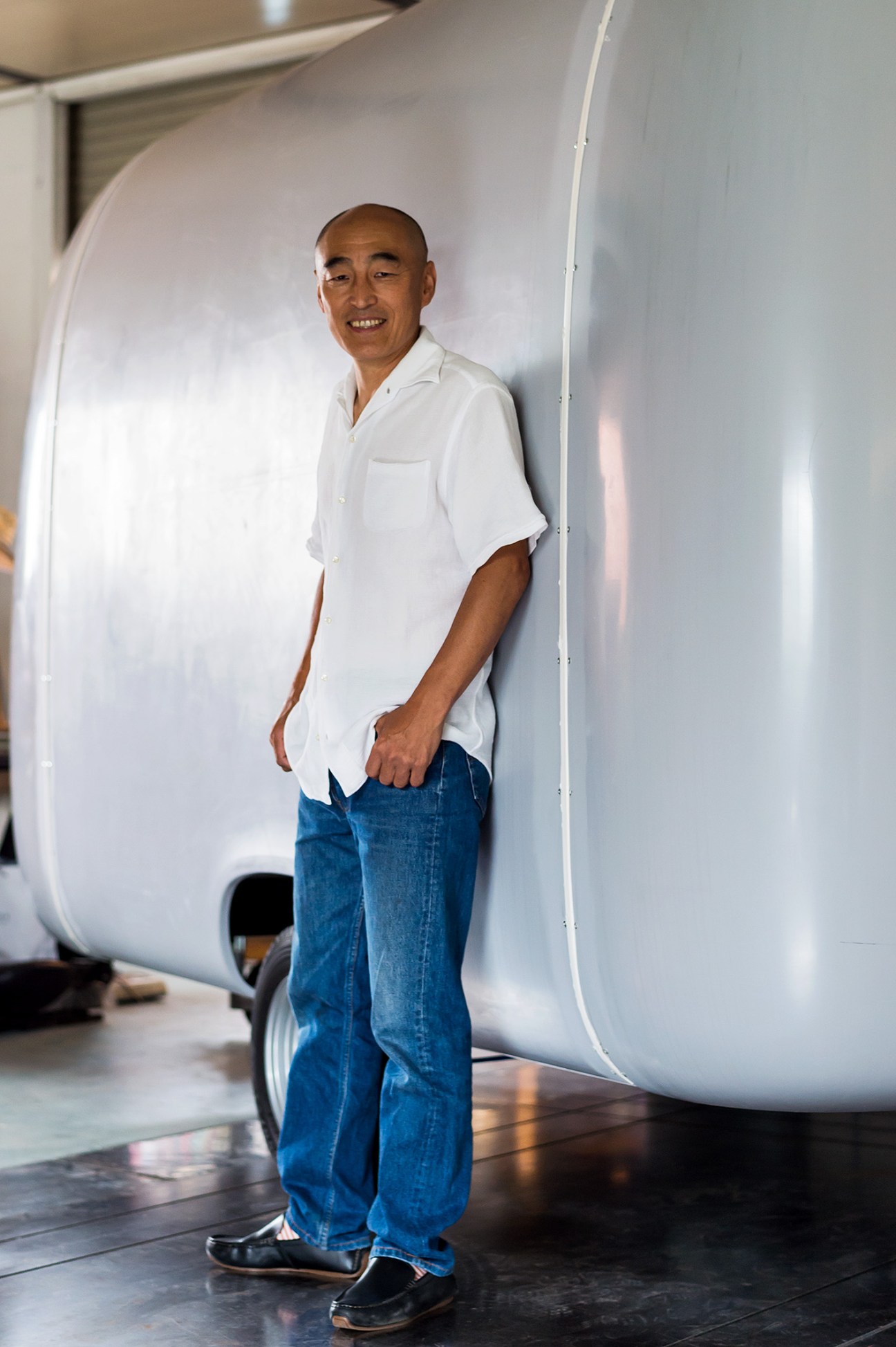 Yoshihiro Tokuda stands inside the Roomette trailer he designed, smiling at the camera.