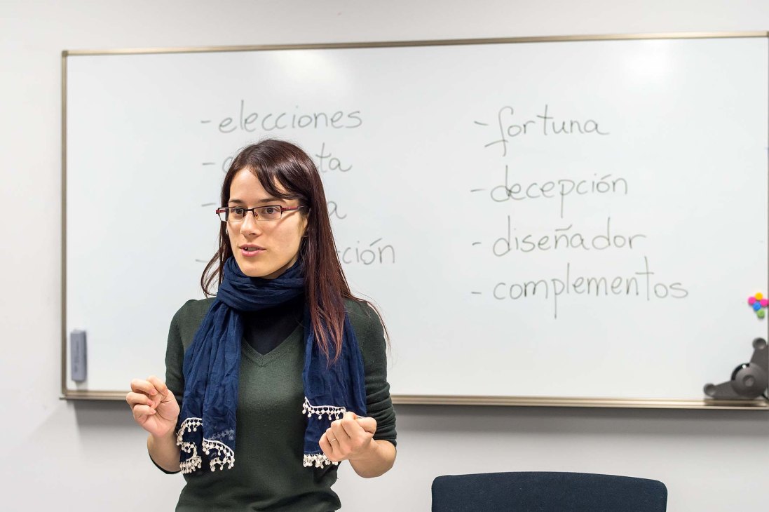 A Spanish teacher named Cristina teaching a language class in front of a whiteboard with Spanish vocabulary words.