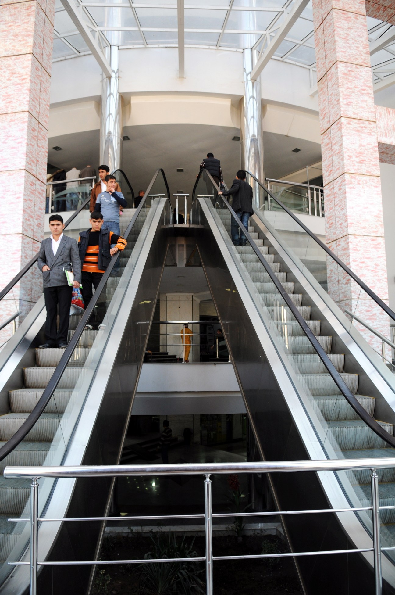 Interior of a modern shopping centre with multiple escalators and shoppers on different levels.