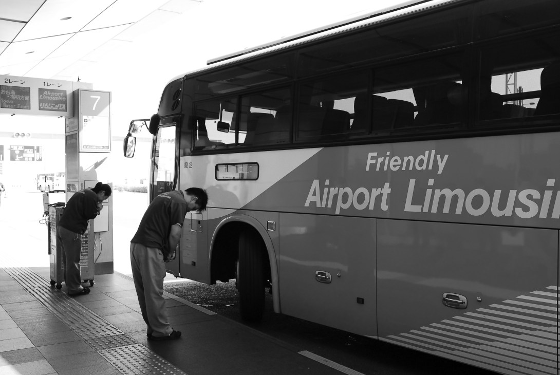 Staff members loading luggage onto a Friendly Airport Limousine bus at Tokyo airport.