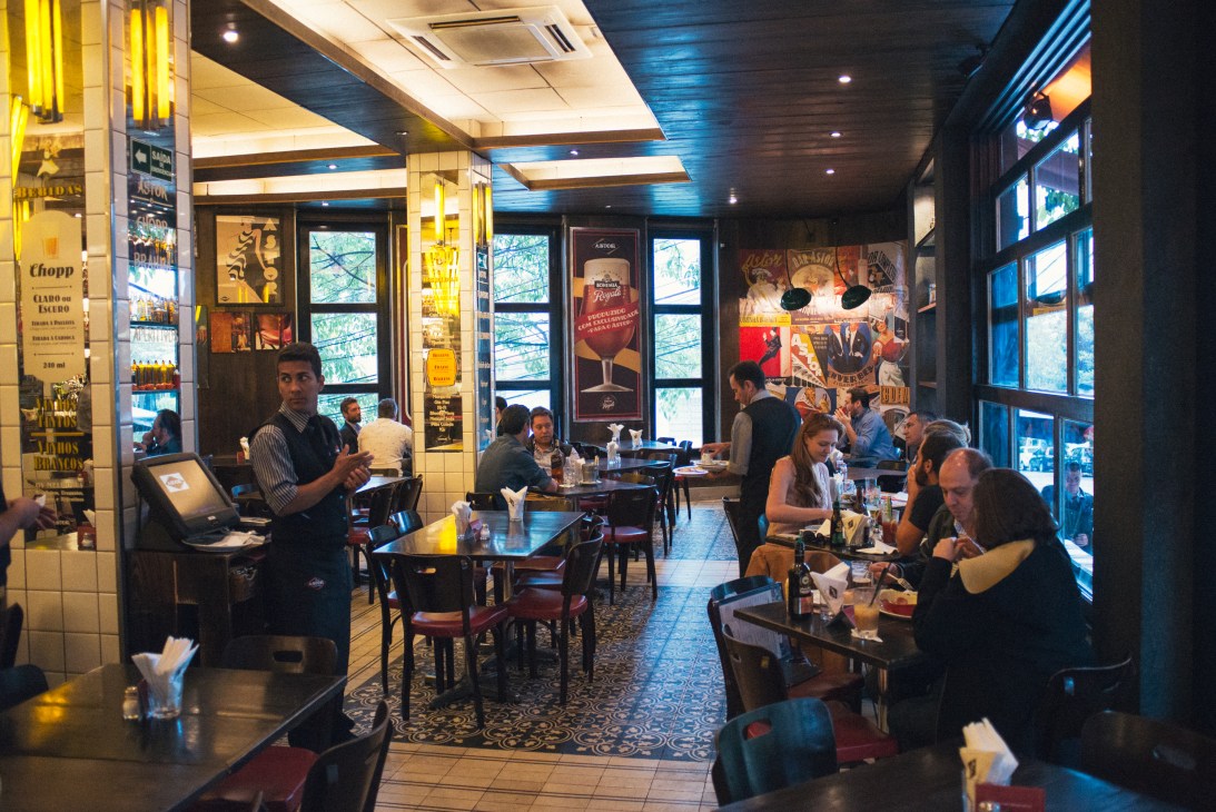 Interior of Bar Astor in São Paulo with diners at tables and vintage posters on walls