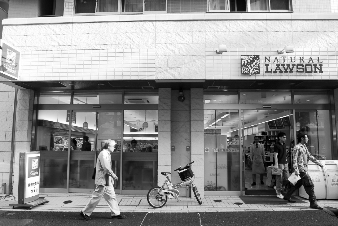 Storefront of Natural Lawson convenience store with customers and a bicycle outside.
