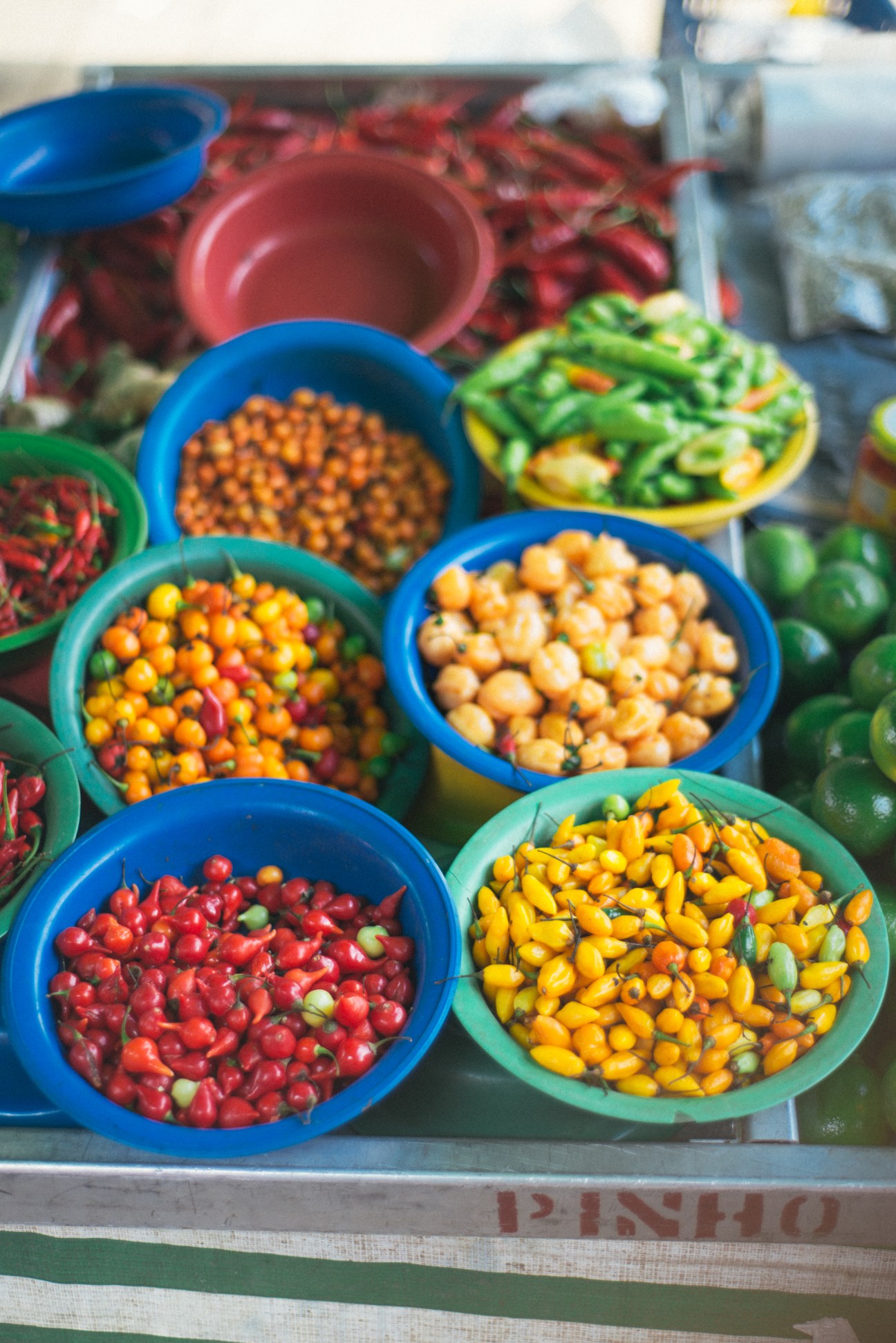 Colorful bowls of fresh produce including red peppers, corn, chickpeas and green beans displayed at São Paulo's market.