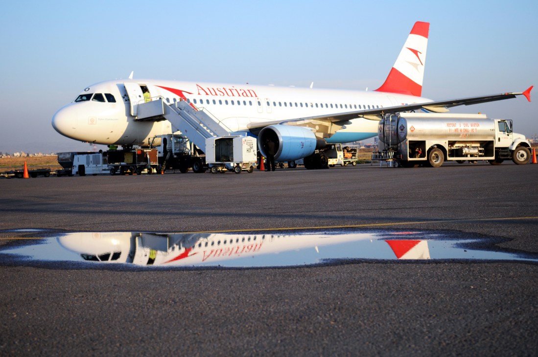 Austrian Airlines aircraft parked on Arbil airport runway with ground support vehicles.