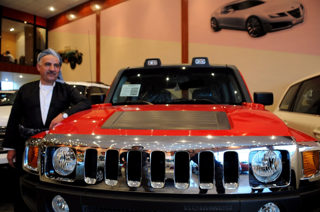 Man standing beside a red Humvee on display in a car showroom with decorative lighting.