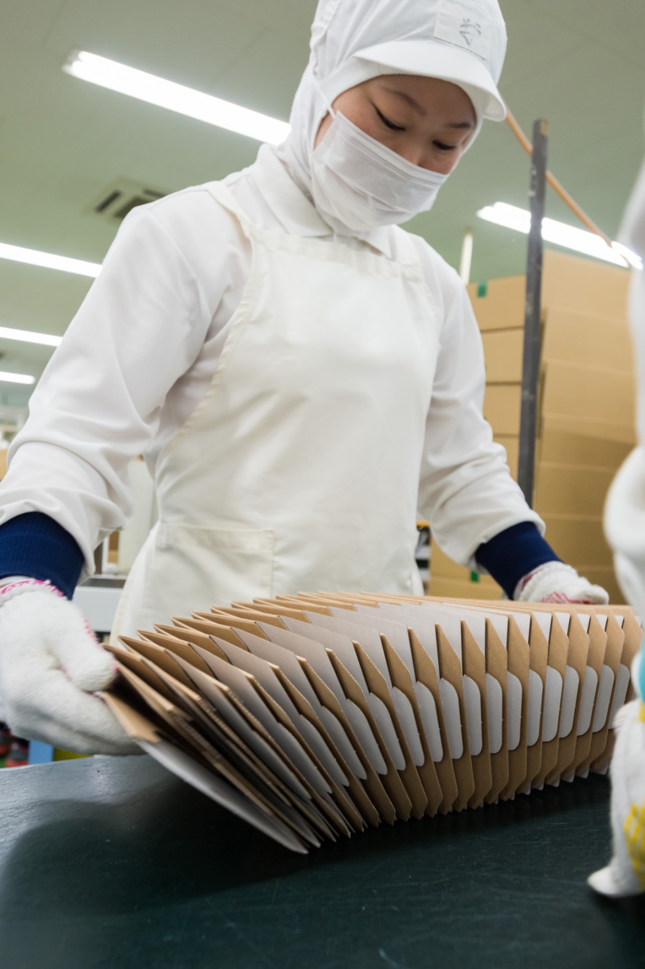 Worker in white uniform and cap handling thin cardboard packaging sheets at Crown Package facility.