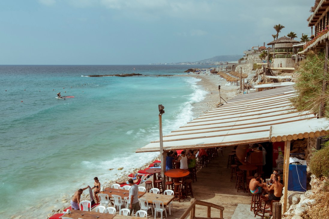 Beachfront cocktail bar Pierre and Friends in Batroun, Lebanon with turquoise Mediterranean waters and coastal cliffs.