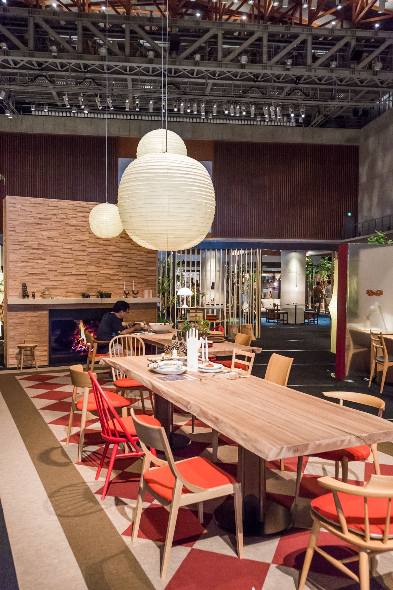 Modern dining area with wooden table, red chairs, fireplace, and oversized cream paper lanterns hanging from ceiling.