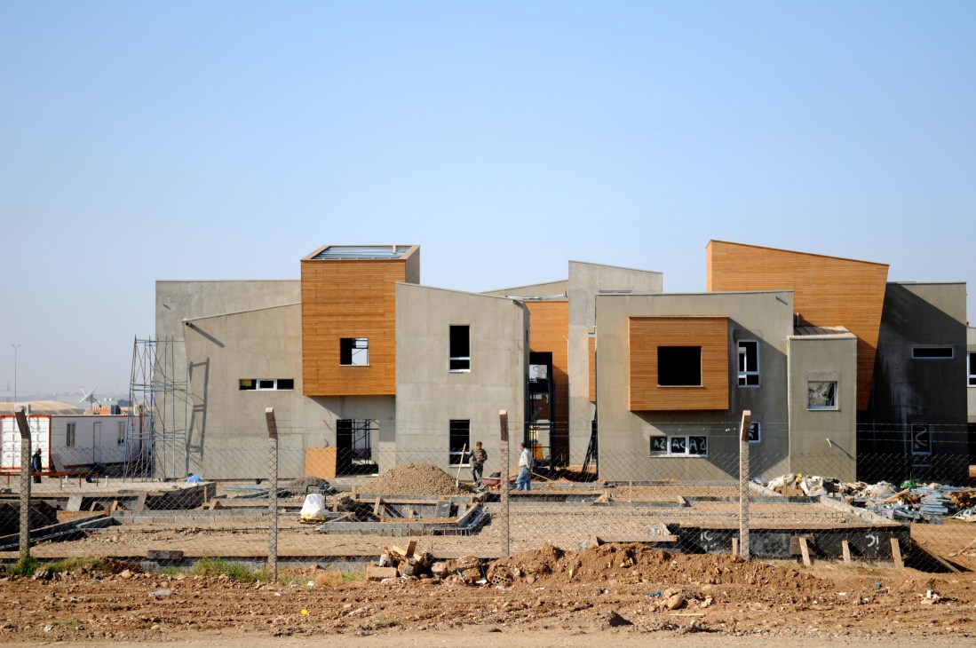 Modern residential houses under construction in Arbil with concrete and wood cladding, surrounded by scaffolding and building materials.