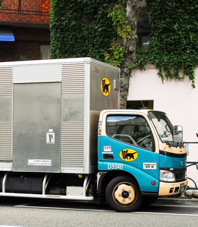 Yamato Holdings delivery truck with blue and white cab and grey refrigerated trailer on urban street.