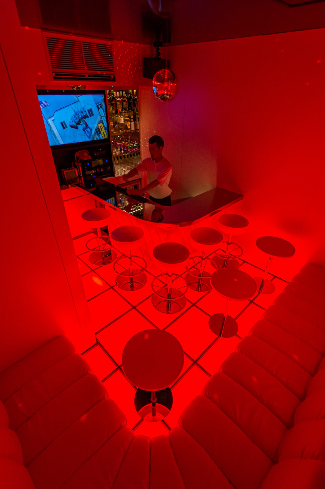 Soundproofed karaoke room with red neon lighting, disco ball, bar seating, and karaoke equipment at Trunk House Tokyo.