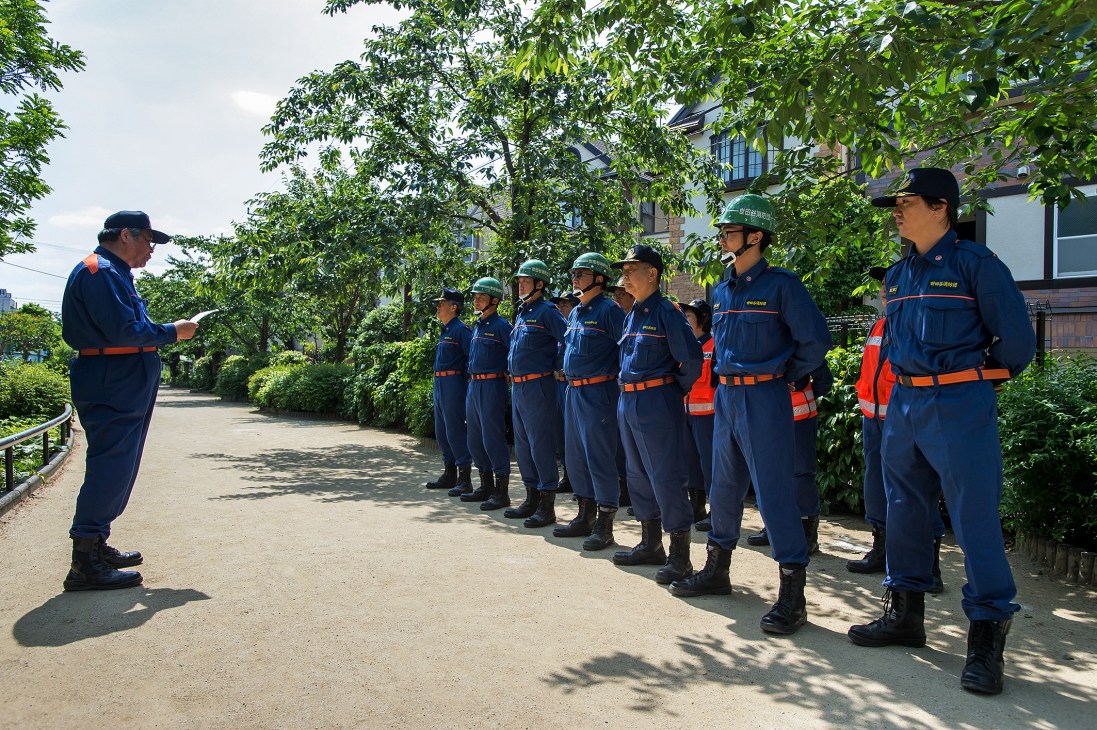 Volunteer firefighters in blue uniforms with orange stripes stand in a line during roll call at a Tokyo fire station.
