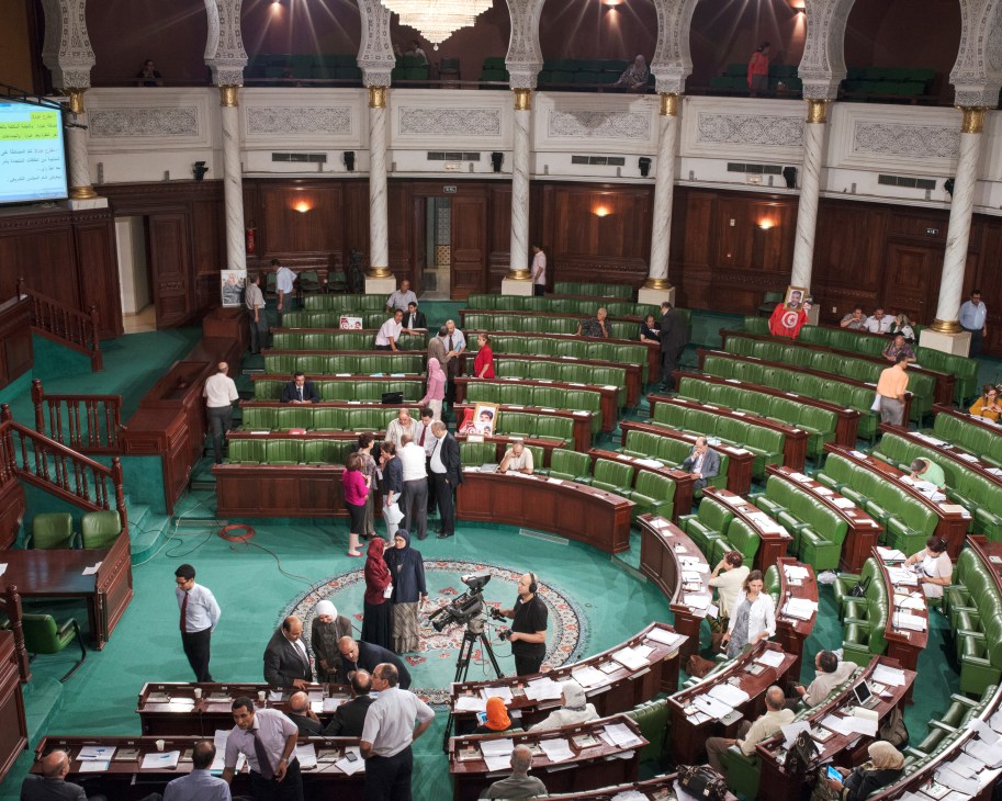 Interior of the Tunisian parliament chamber with green seats and ornate white columns during a session.