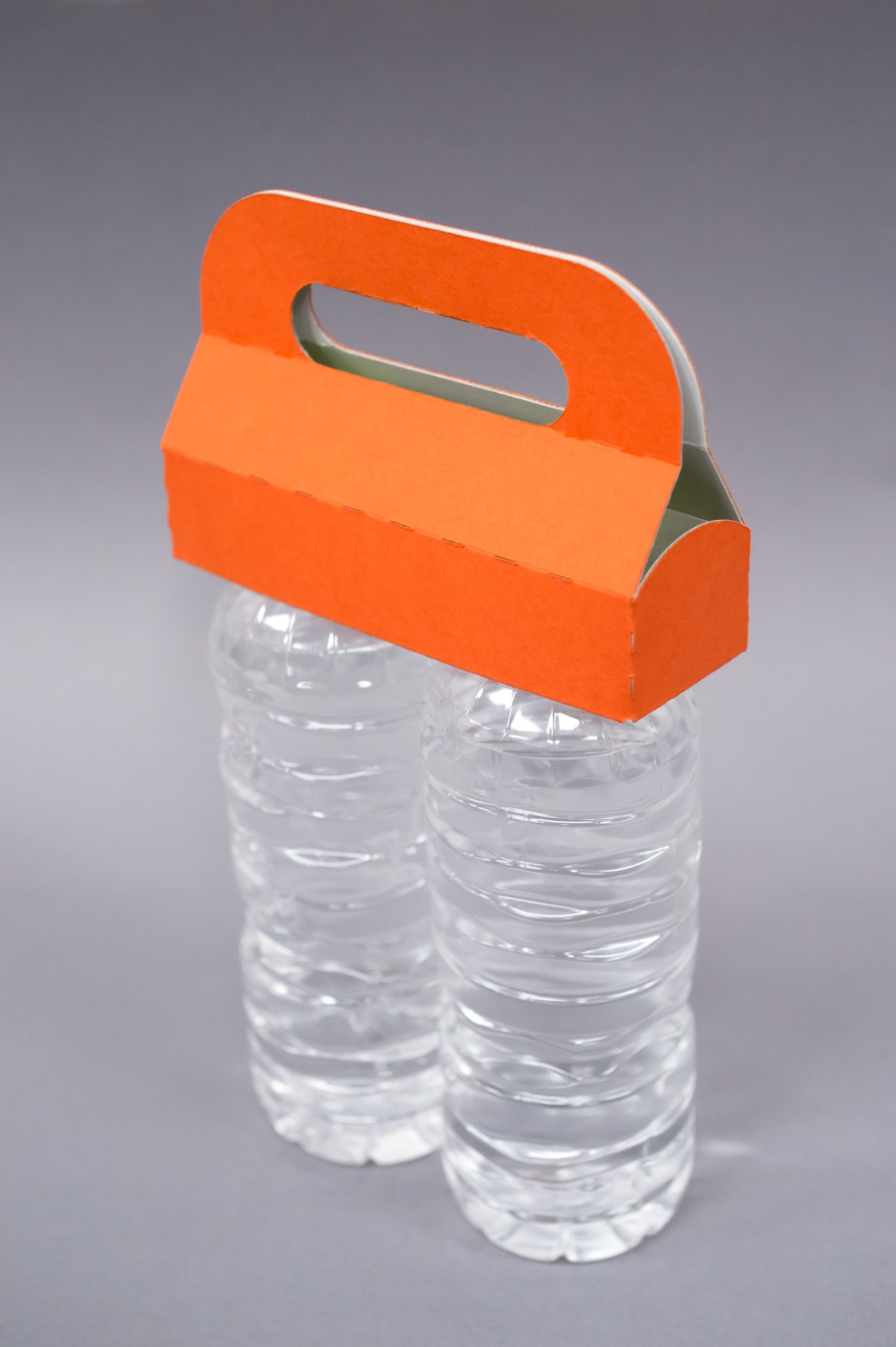 Orange cardboard carrier holding two clear plastic bottles against gray background.