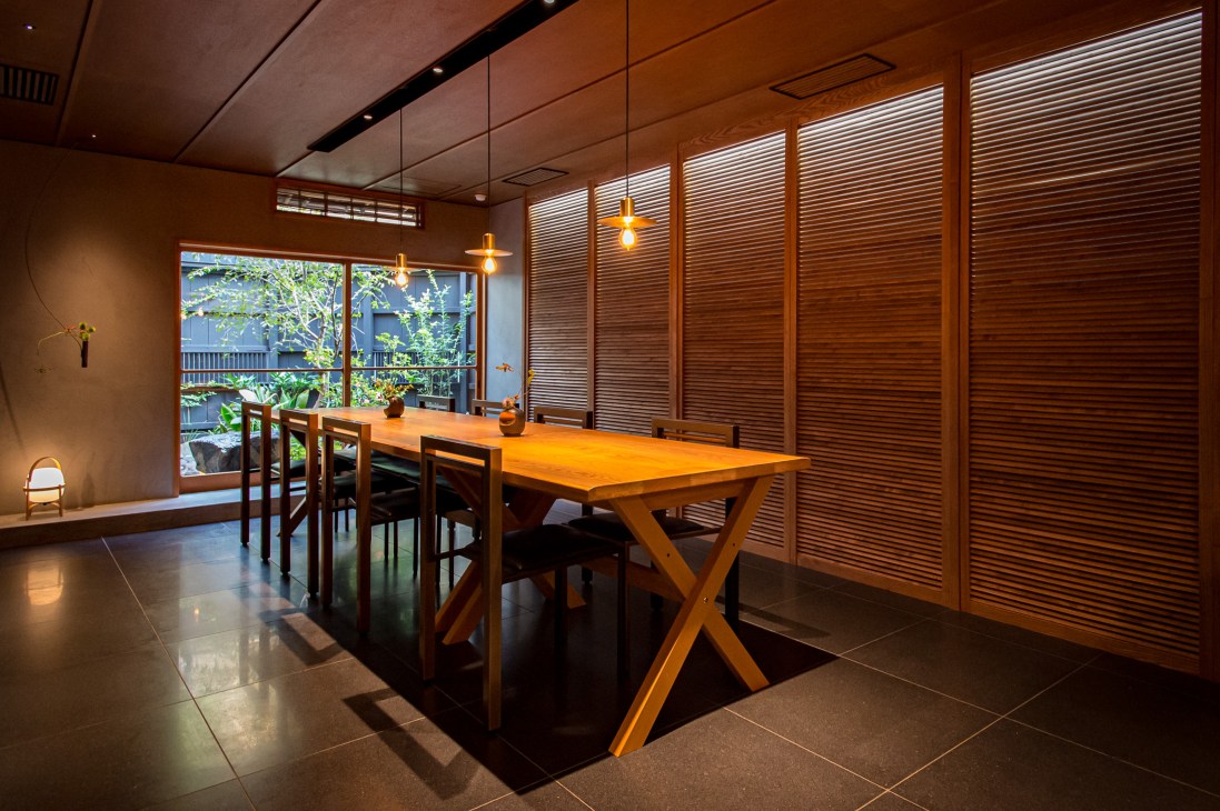 Wooden dining table with chairs in a modern Japanese interior with paper screens and courtyard views.